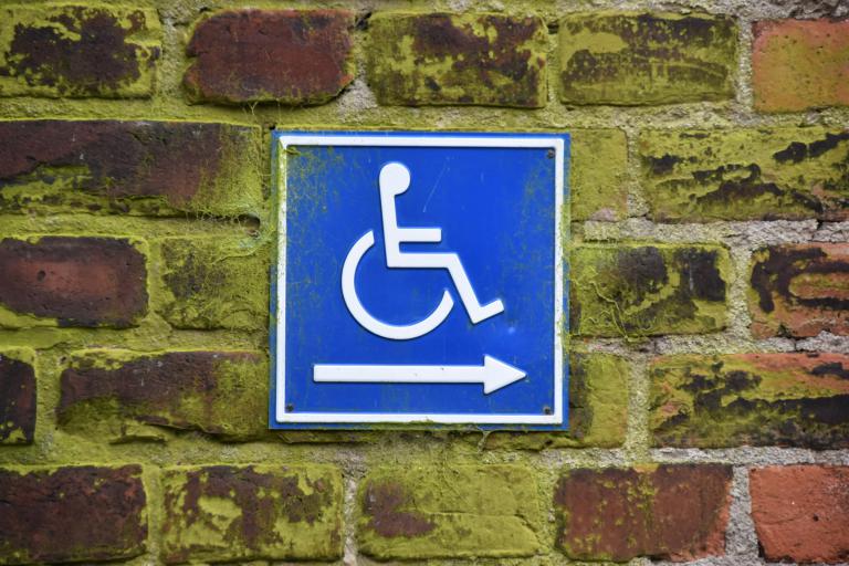 A blue and white wheelchair sign on a brick wall with an arrow pointing to the right