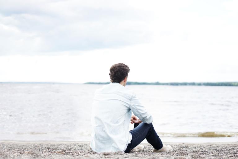 Student with his back to the camera sitting on the beach looking out to sea