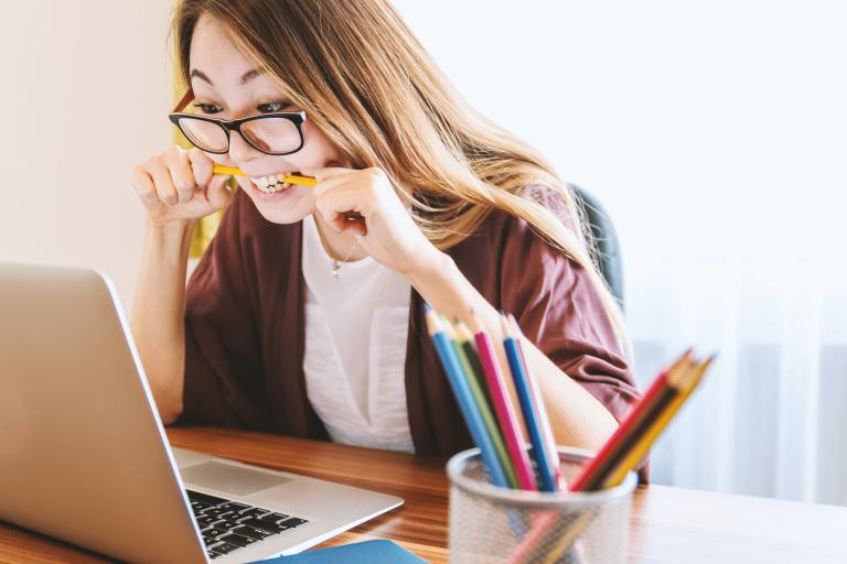 Student looking at her laptop chewing her pencil