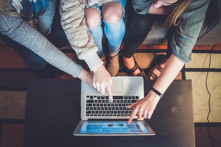 Three students sitting in front of a laptop pointing to the screen