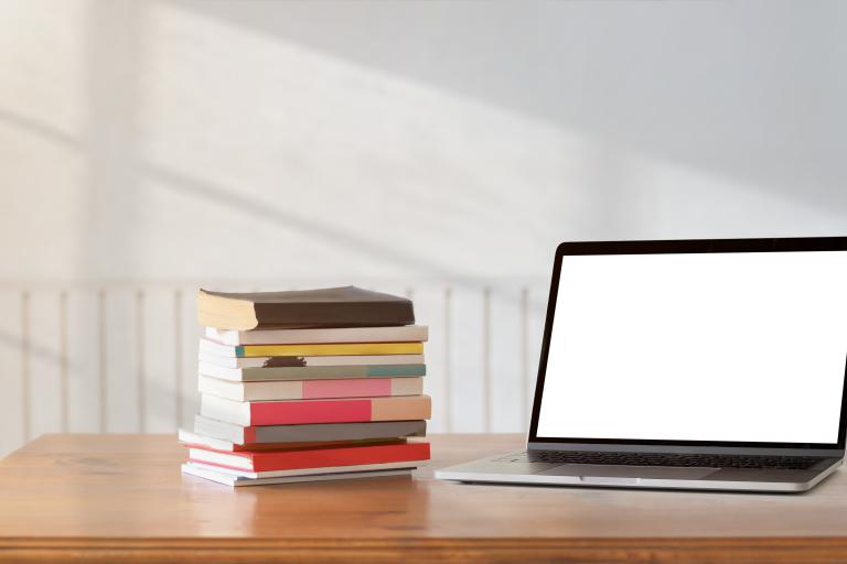 Photo of a pile of books and a laptop on a desk