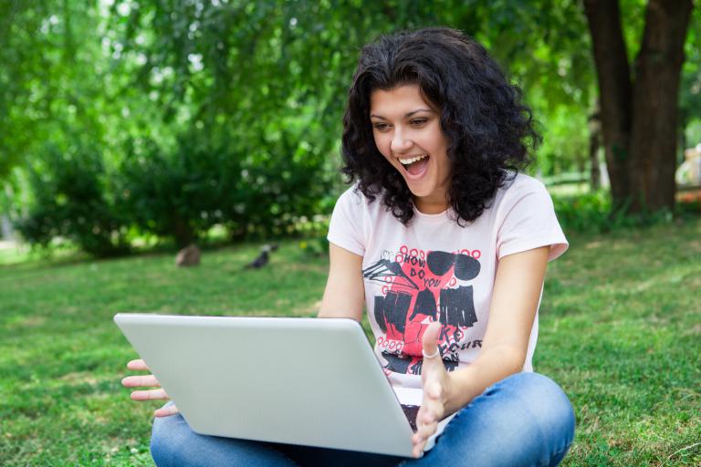 Smiling girl in a park looking at a laptop