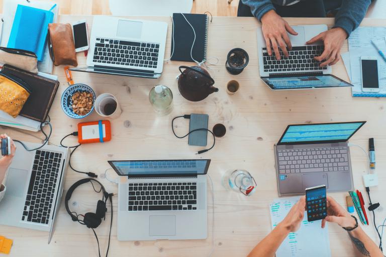 Group of laptop users sitting at a table with only hands and devices visible