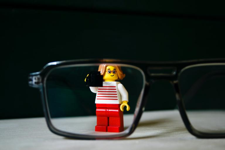 Lego figure standing behind a pair of glasses.