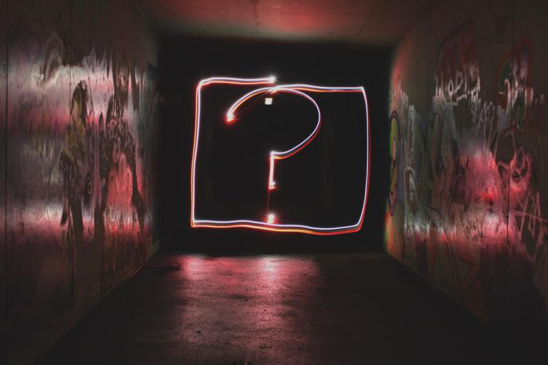 Abstract neon sign showing a question mark against a blurred background.