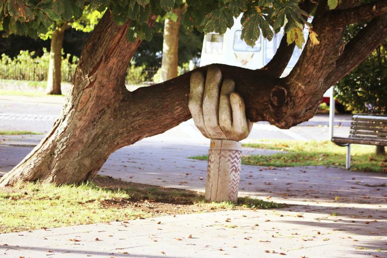 Large wooden hand sculpture holding up a sagging tree trunk.