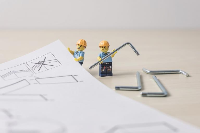 Two Lego people reading flat pack assembly instructions.