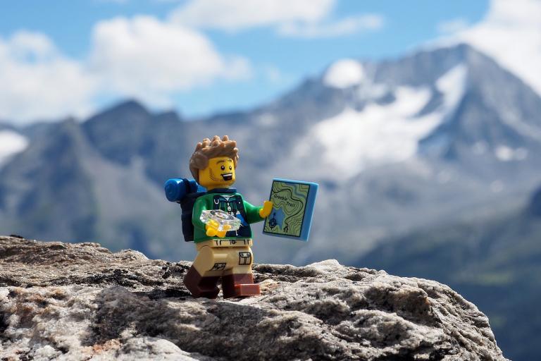 Photo of a Lego person walking in the mountains holding a map.