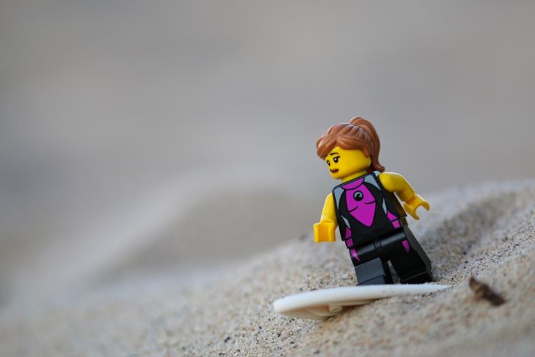 Photo of a Lego minifigure surfing in the sand.