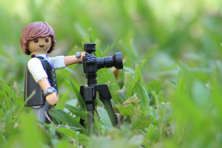 Lego minifigure with camera in grass.