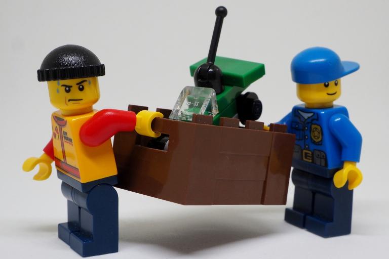 Two Lego minifigures carrying a box of equipment.